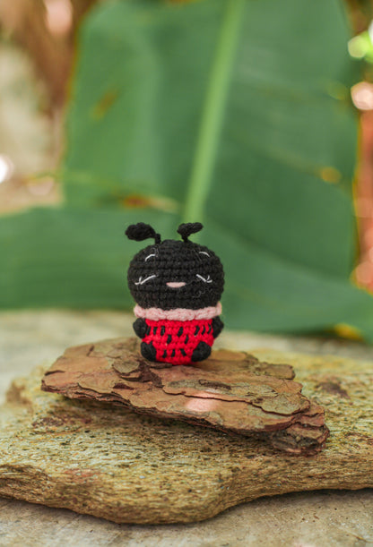 Small crochet ladybug mini with a black head and red spotted body sitting on bark on a rock outdoors