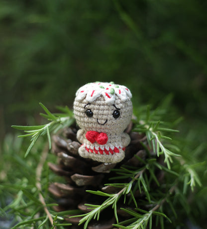 Crochet reindeer mini with a white sprinkle-flecked cap and a red heart, on a pine cone among greenery