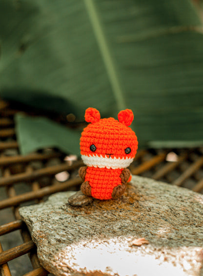 Orange crochet fox mini with a cream-white muzzle and brown paws, sitting on a stone outdoors