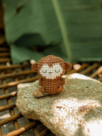 Brown crochet monkey mini with a cream face sitting on a stone outdoors, woven basket behind