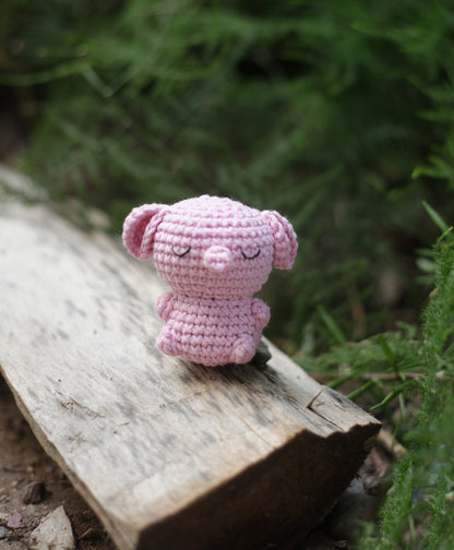 Small pink crochet elephant mini with big ears sitting on a piece of driftwood outdoors