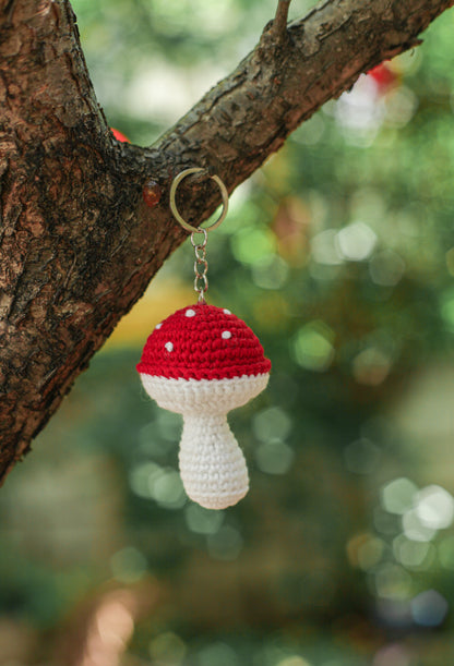 Red and white spotted crochet mushroom keychain hanging from a tree branch on a metal key ring