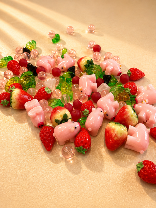 Berrybell bead box mix spread on cream fabric — pink pig beads, strawberry beads and pink and red beads.