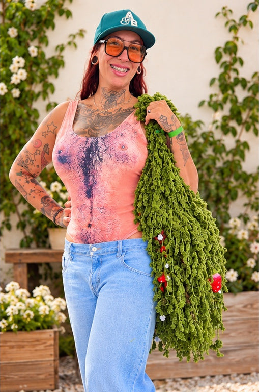 Customer in a pink top and teal cap wearing the Strawberry Moss crochet foraging bag in a garden setting