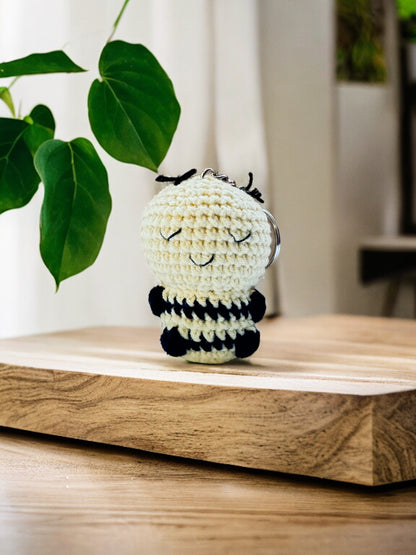 Cream crochet bee with black stripes and a smiling face on a wooden board with green leaves