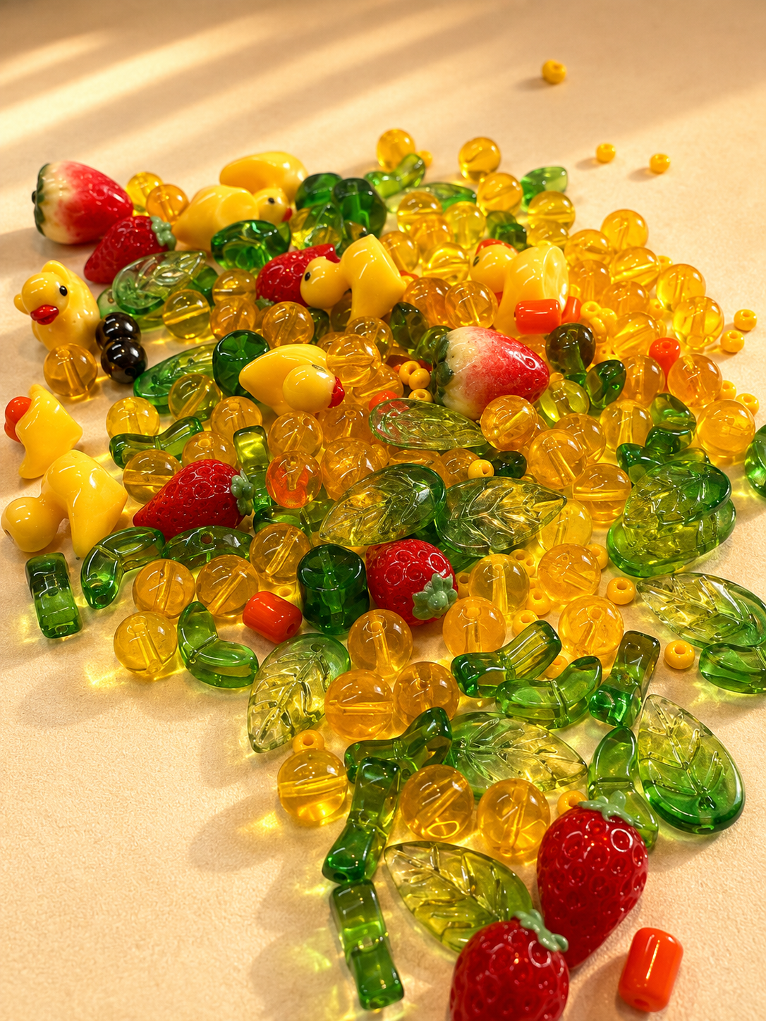 Sunny bead box mix spread on cream fabric — yellow duck beads, leaf beads and strawberry beads.
